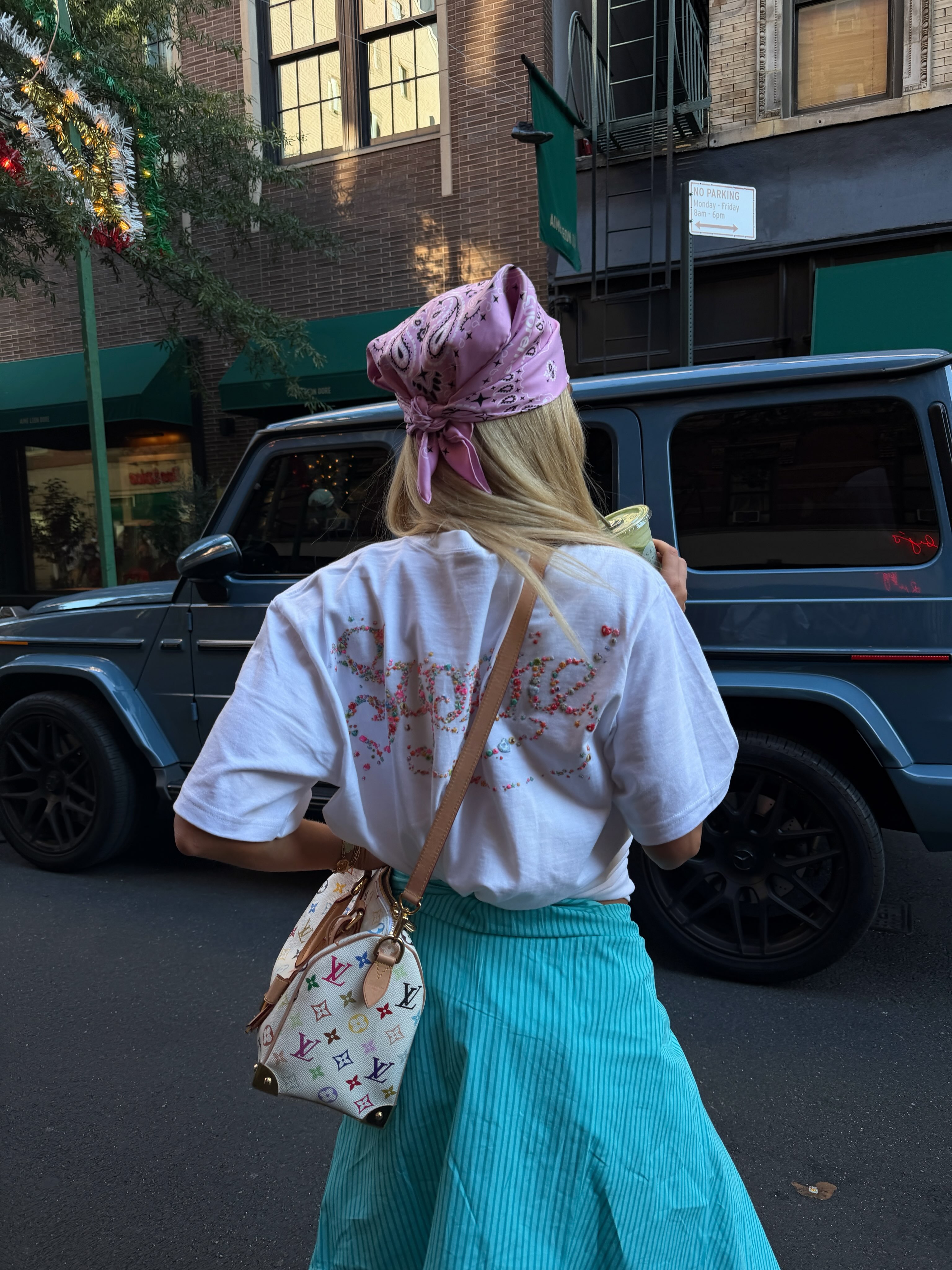 Back view of a woman wearing a white T-shirt and bright blue pleated skirt.